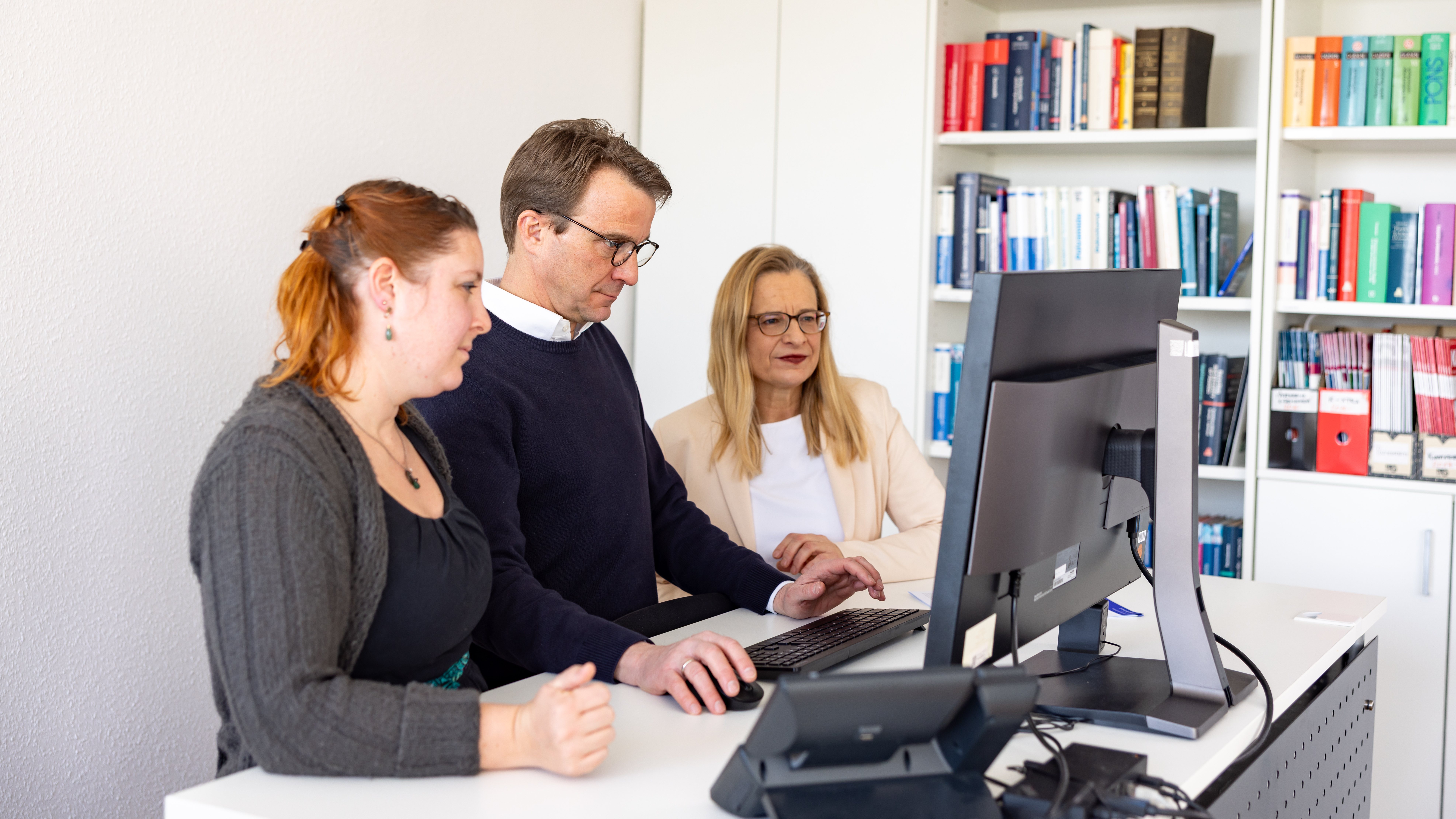 Drei Mitarbeitende arbeiten gemeinsam an einem Bildschirmarbeitsplatz